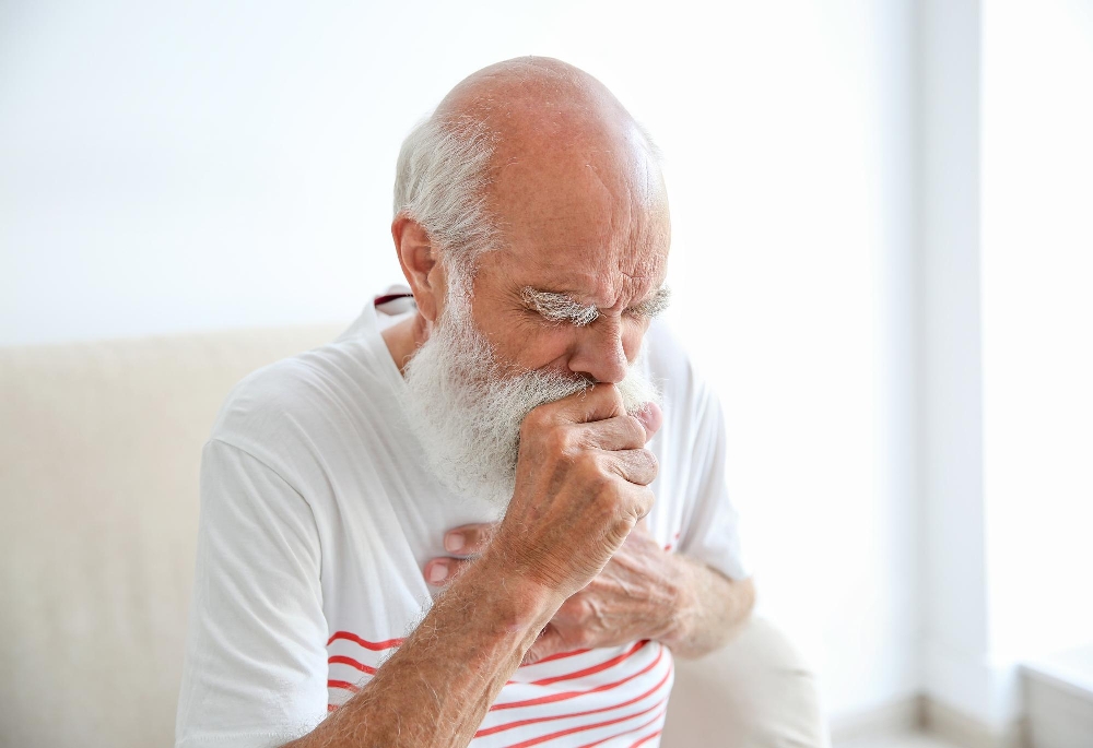 Older man coughing into his fist, having trouble swallowing, wearing a white striped shirt 
